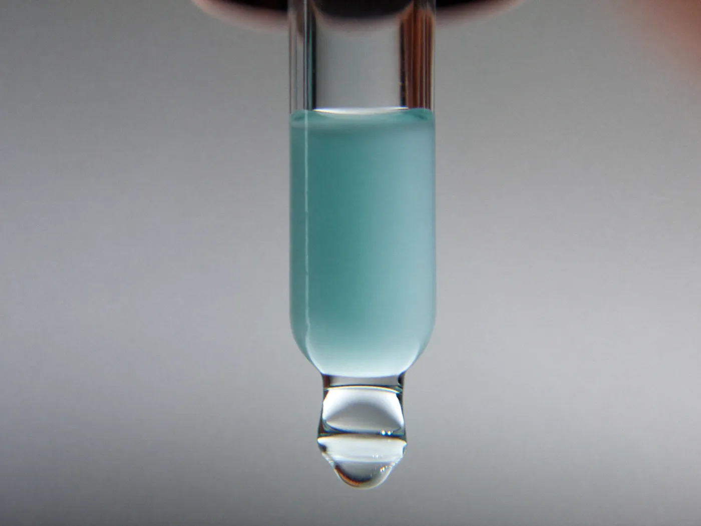 Macro do conta-gotas de vidro com uma gota de sérum azul-claro prestes a cair